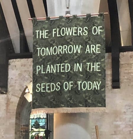 Poster hanging from a ceiling saying 'The flowers of tomorrow are planted in the seeds of today'